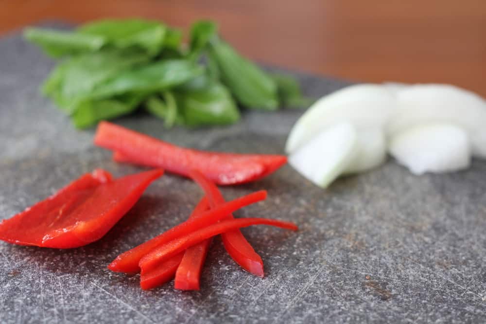 peppers, onions, and basil on a grey cutting board