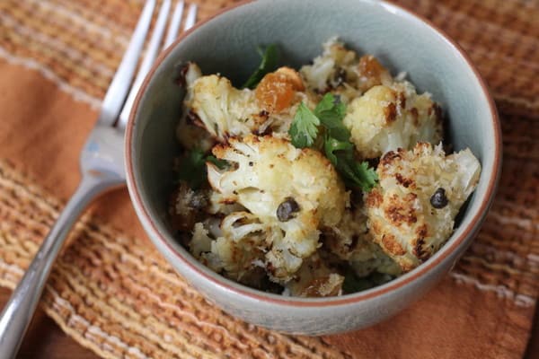 a bowl of cauliflower and capers on a brown placemat