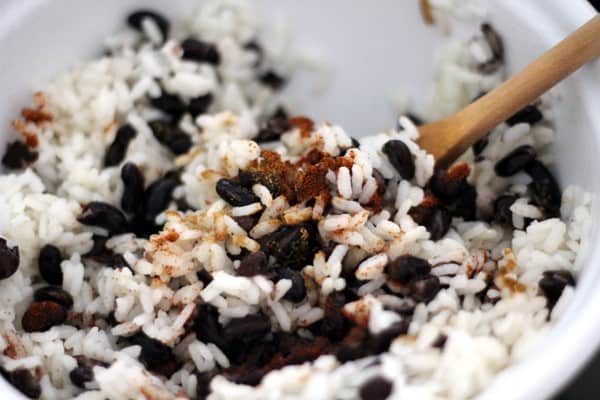 stirring rice and black beans in a white mixing bowl