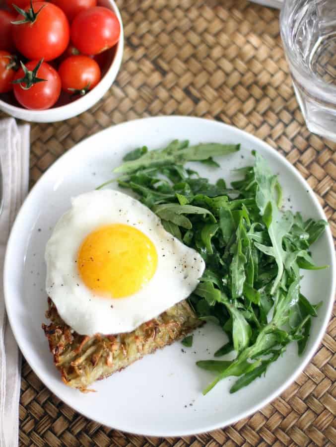 hash browns with a fried egg and arugula on a white plate